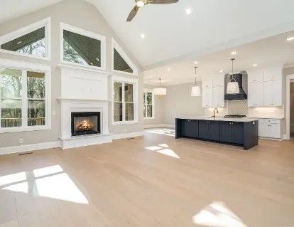 Spacious, light-filled living space with fireplace, windows, kitchen island, and hardwood floors.