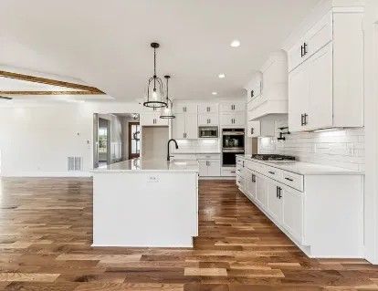 Spacious white kitchen with island, cabinets, appliances, dark hardware, and wood flooring.
