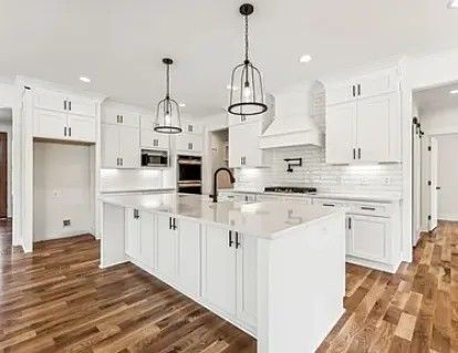 Modern white kitchen with island, dark hardware, and hardwood floors.