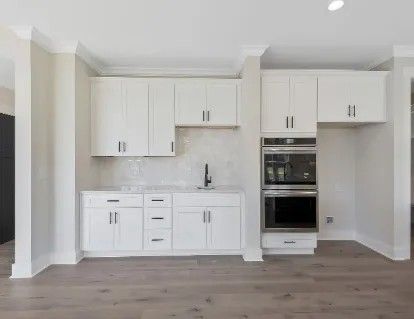 White kitchen area with cabinets, a sink, and built-in double oven on light wood floors.