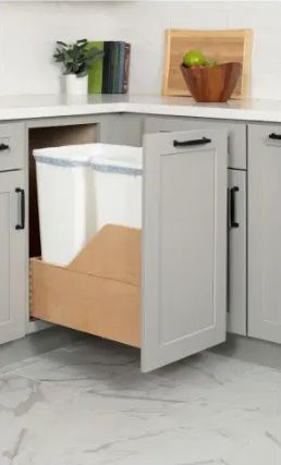 Gray kitchen cabinet with pull-out drawer holding two white trash bins. Corner setting.