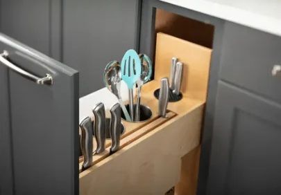 Open gray kitchen cabinet with a pull-out knife and utensil holder.