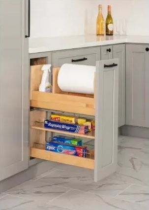 A pull-out kitchen cabinet with cleaning supplies, paper towels, and food wrap organized on shelves.