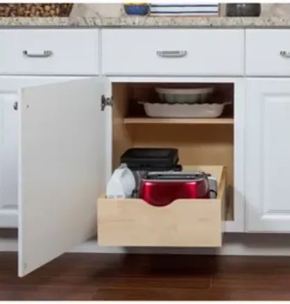 Open white kitchen cabinet with pull-out drawer holding appliances. Beige shelf above with bowls.
