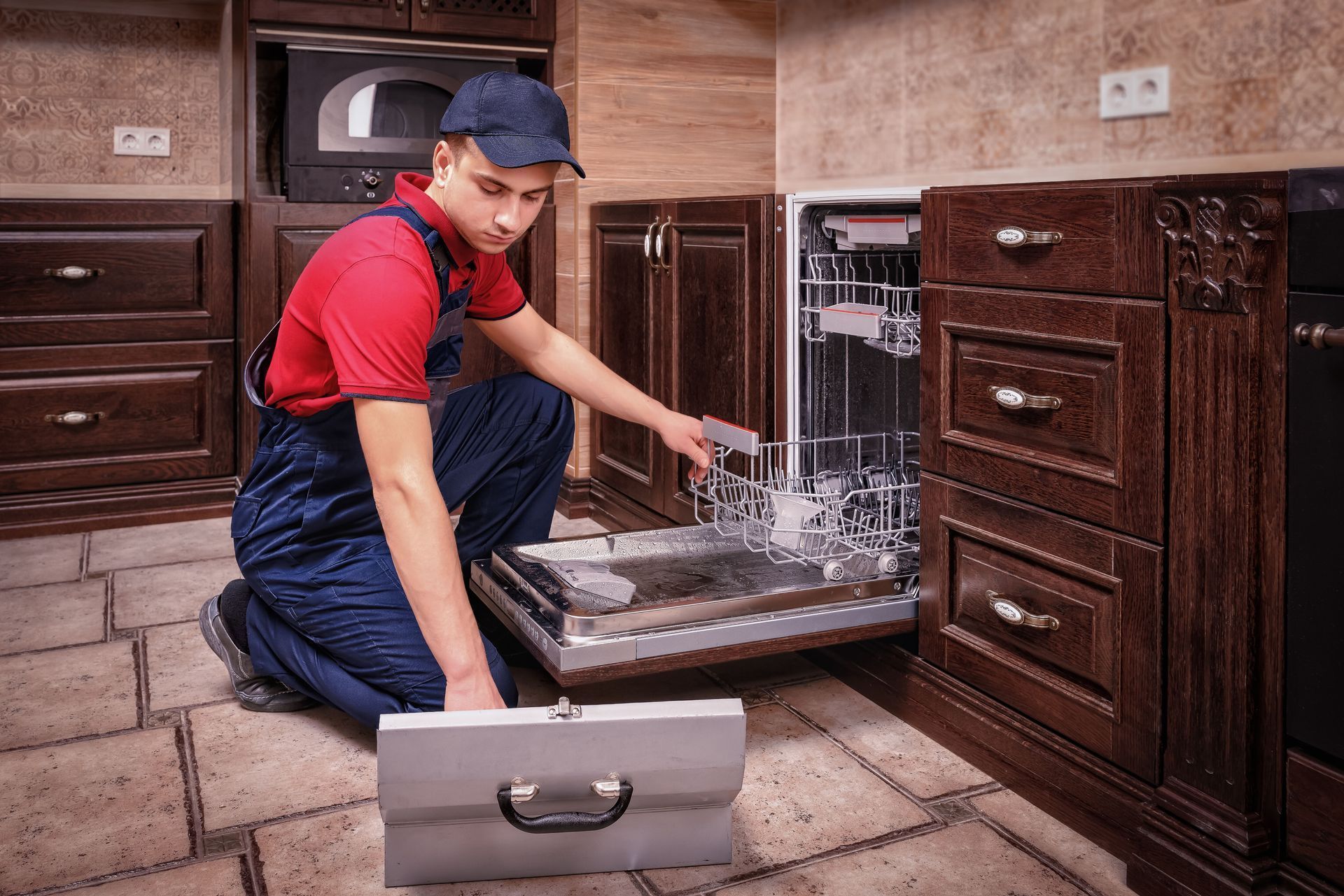 Person in red shirt and blue cap loading a dishwasher in a wooden kitchen.