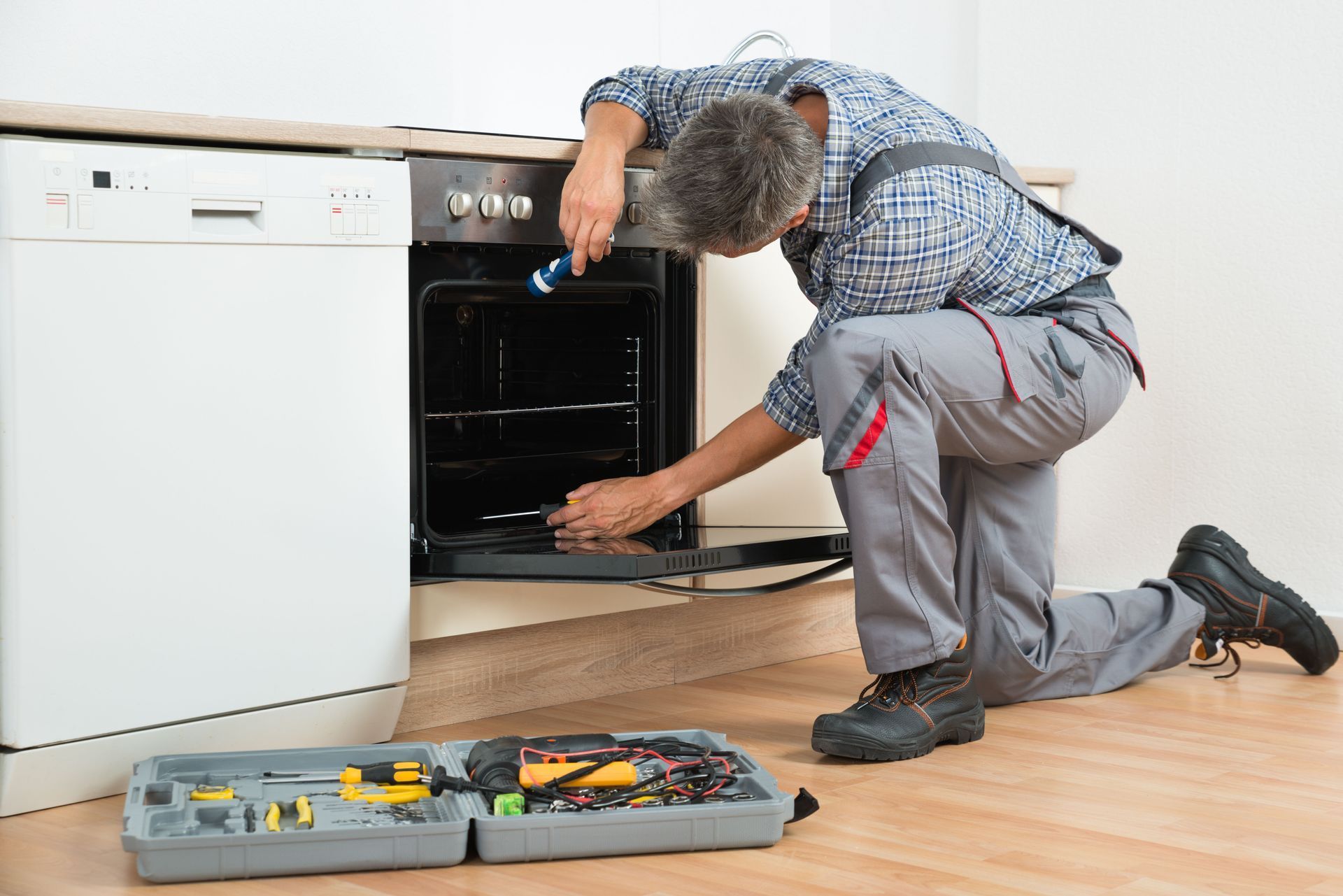 Technician kneels by an open dishwasher, using tools on the kitchen floor.