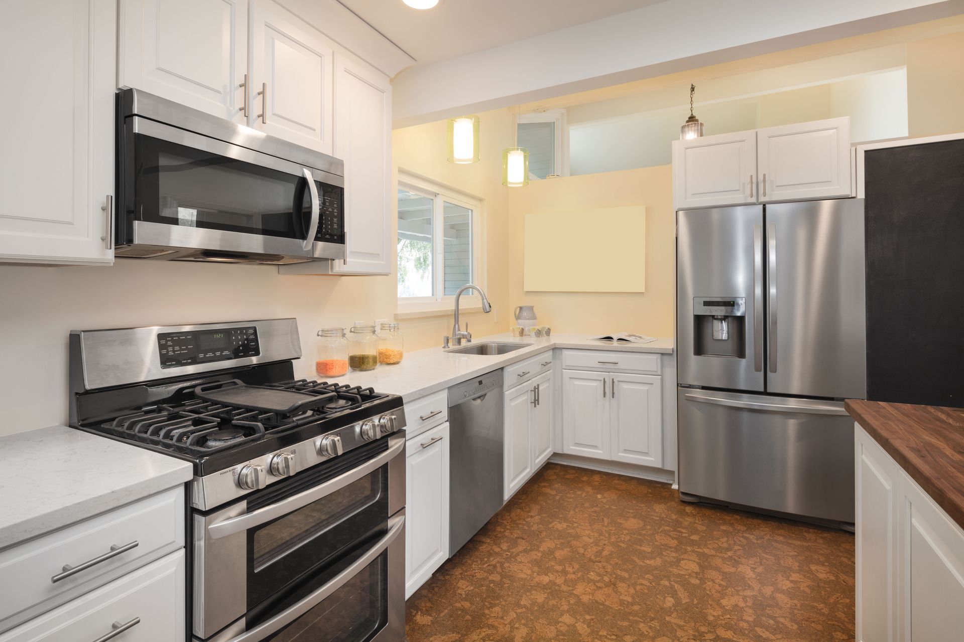 Bright modern kitchen with stainless steel appliances, white cabinets, and brown flooring
