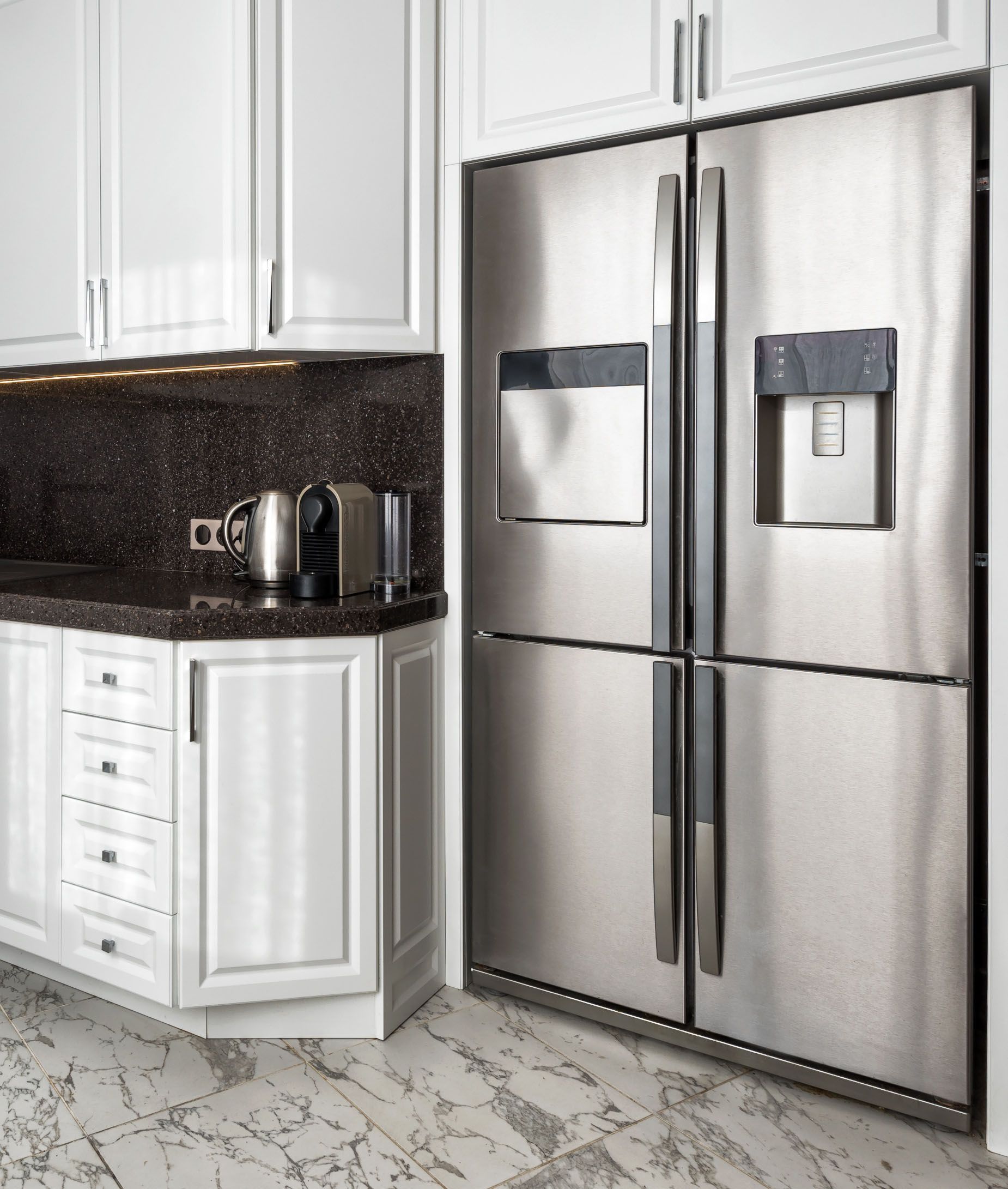 Modern kitchen with stainless steel French-door refrigerator beside white cabinets and marble flooring