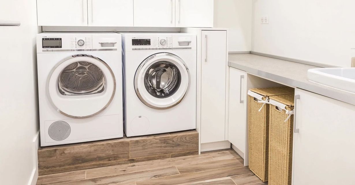 Laundry room with two front-loading washers beside white cabinets and a countertop.