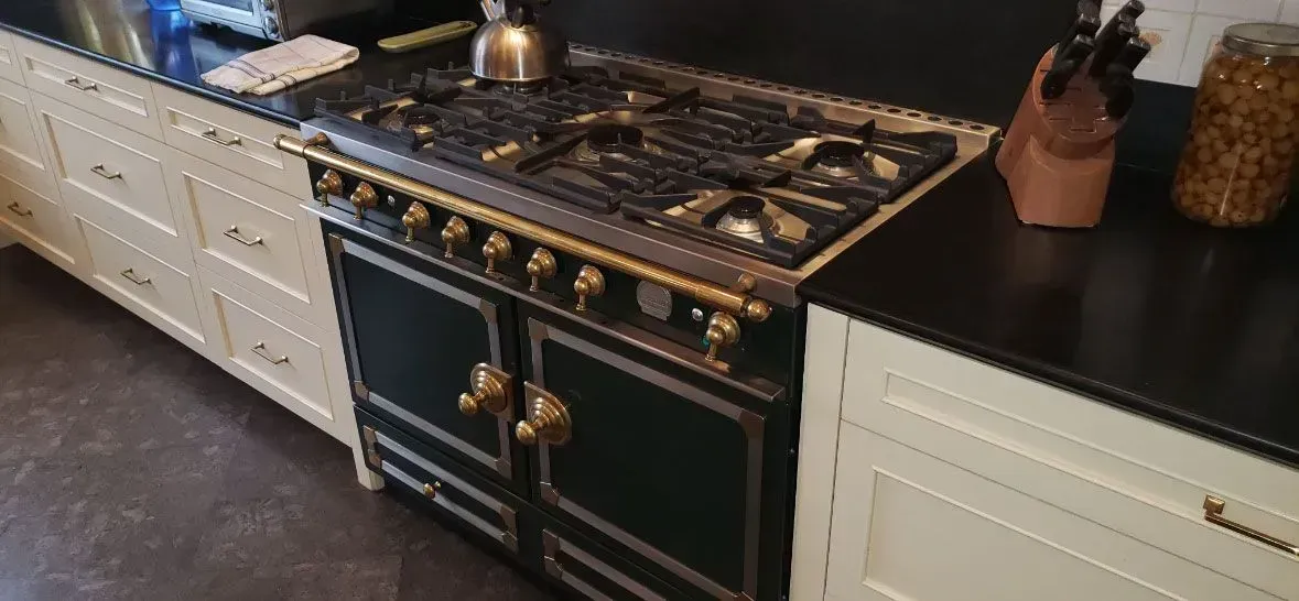 Kitchen with a black-and-gold range between white cabinets and dark countertops.