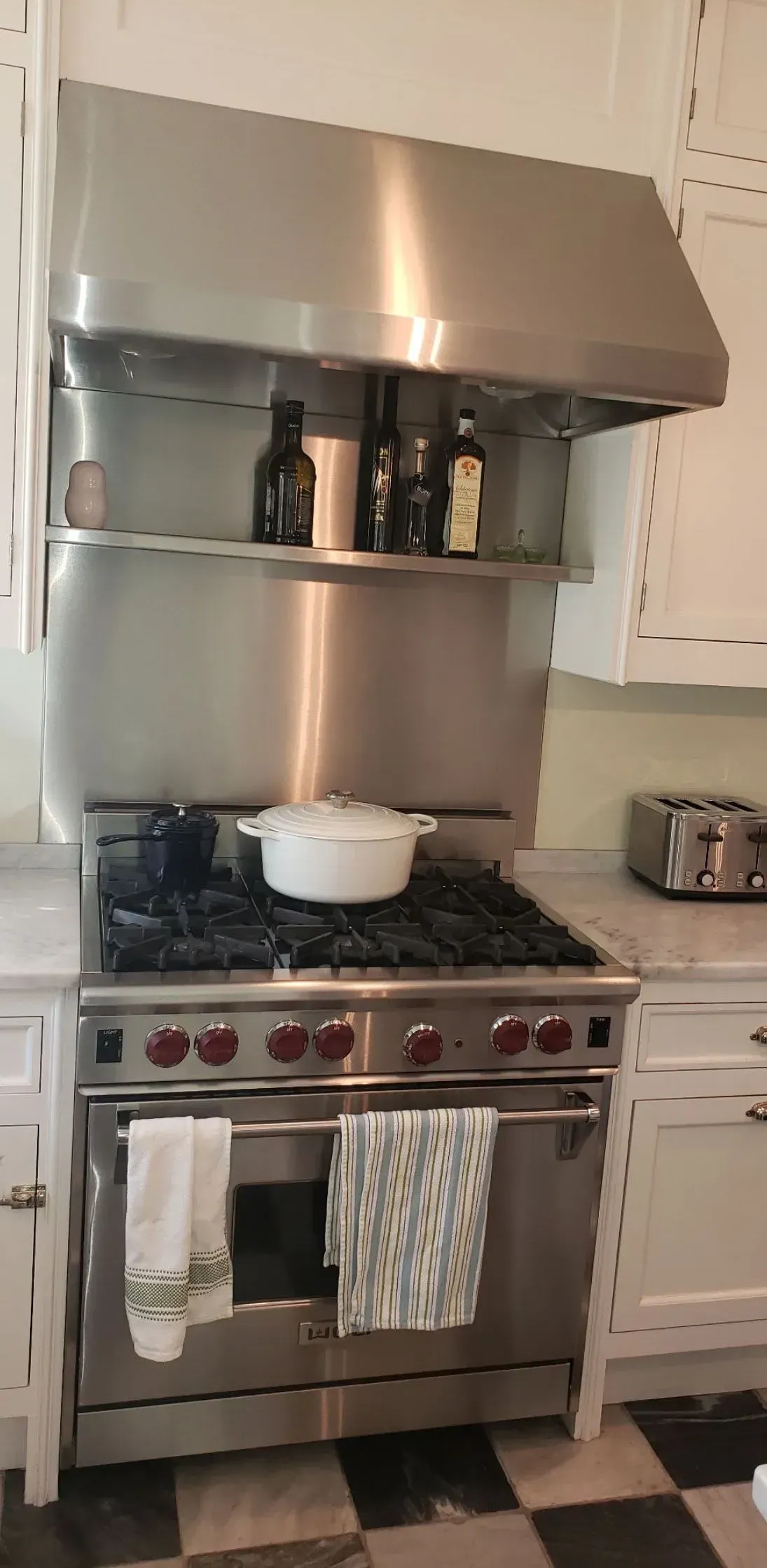 Stainless steel stove and hood in a white kitchen, with a pot on the burner and towels hanging on the oven door.