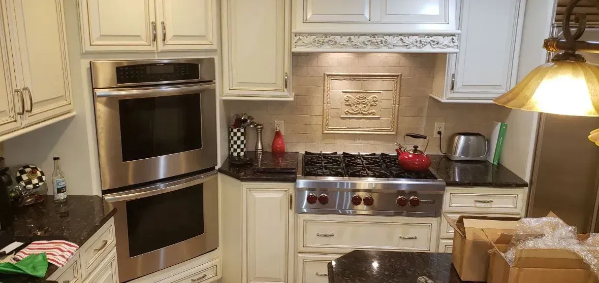Bright kitchen with cream cabinets, stainless steel oven, stove, and hanging pendant light.