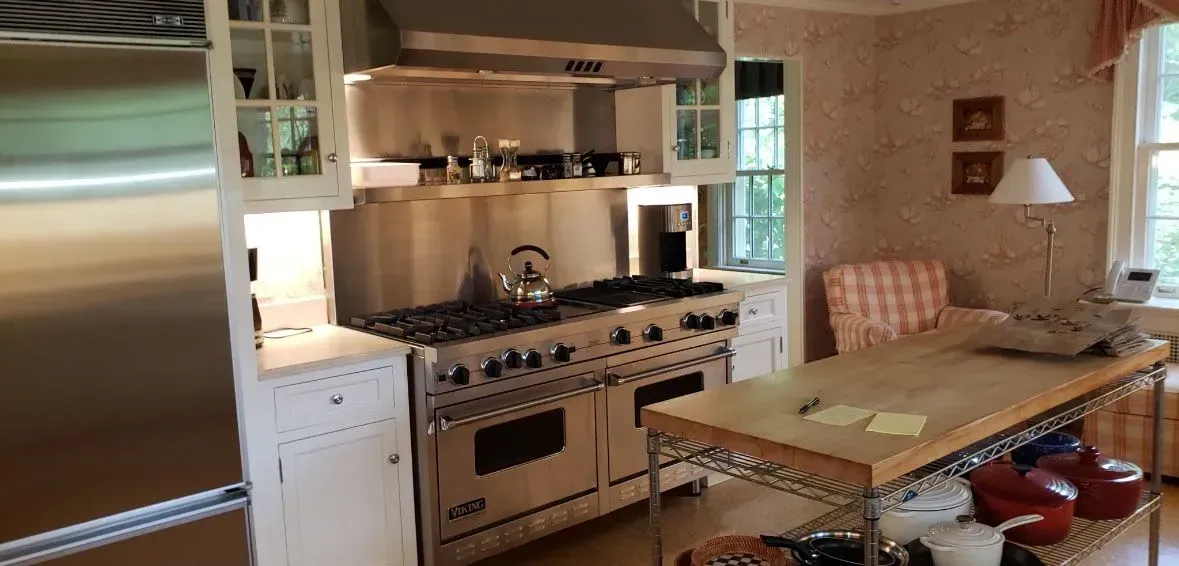 Cozy kitchen with stainless steel stove and refrigerator, wood island table, and pink chairs near a window.