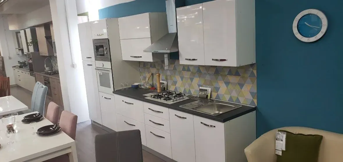 Modern kitchen with white cabinets, black countertop, blue accent wall, and a wall clock