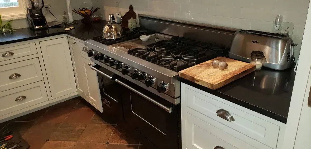 Modern kitchen with white cabinets, black countertop, gas stove, and cutting board beside a toaster.