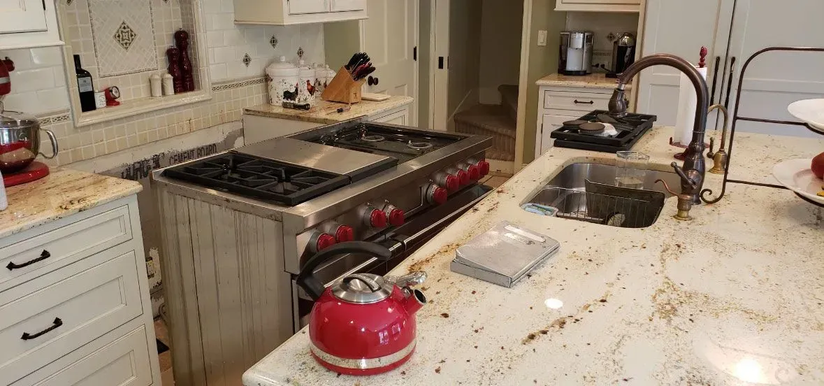 Messy kitchen with splattered countertop, red kettle, and a stove surrounded by debris
