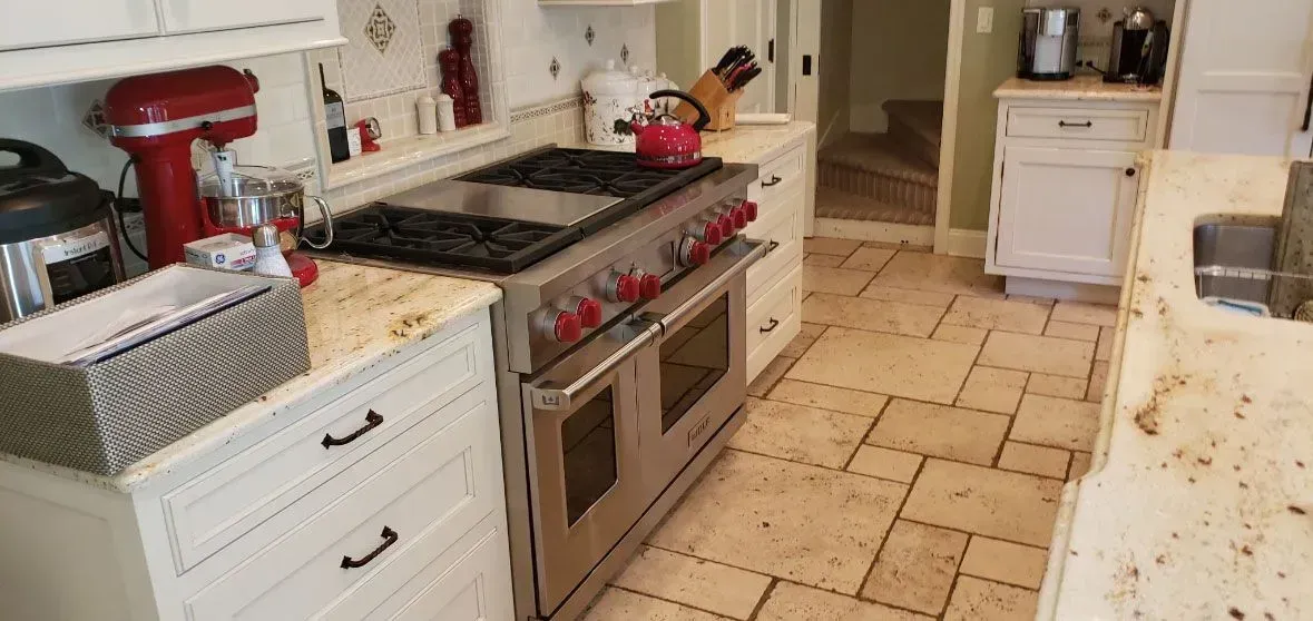 Bright kitchen with red stove, white cabinets, marble counters, and tiled floor