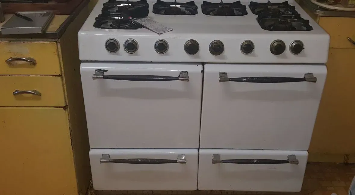 White gas stove with four burners and oven, between wooden cabinets in a kitchen.