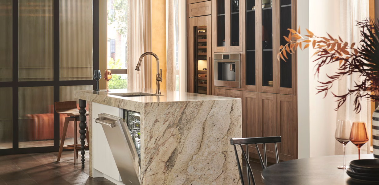 Modern kitchen with marble island, wooden cabinets, glass doors, and a potted plant by a window.