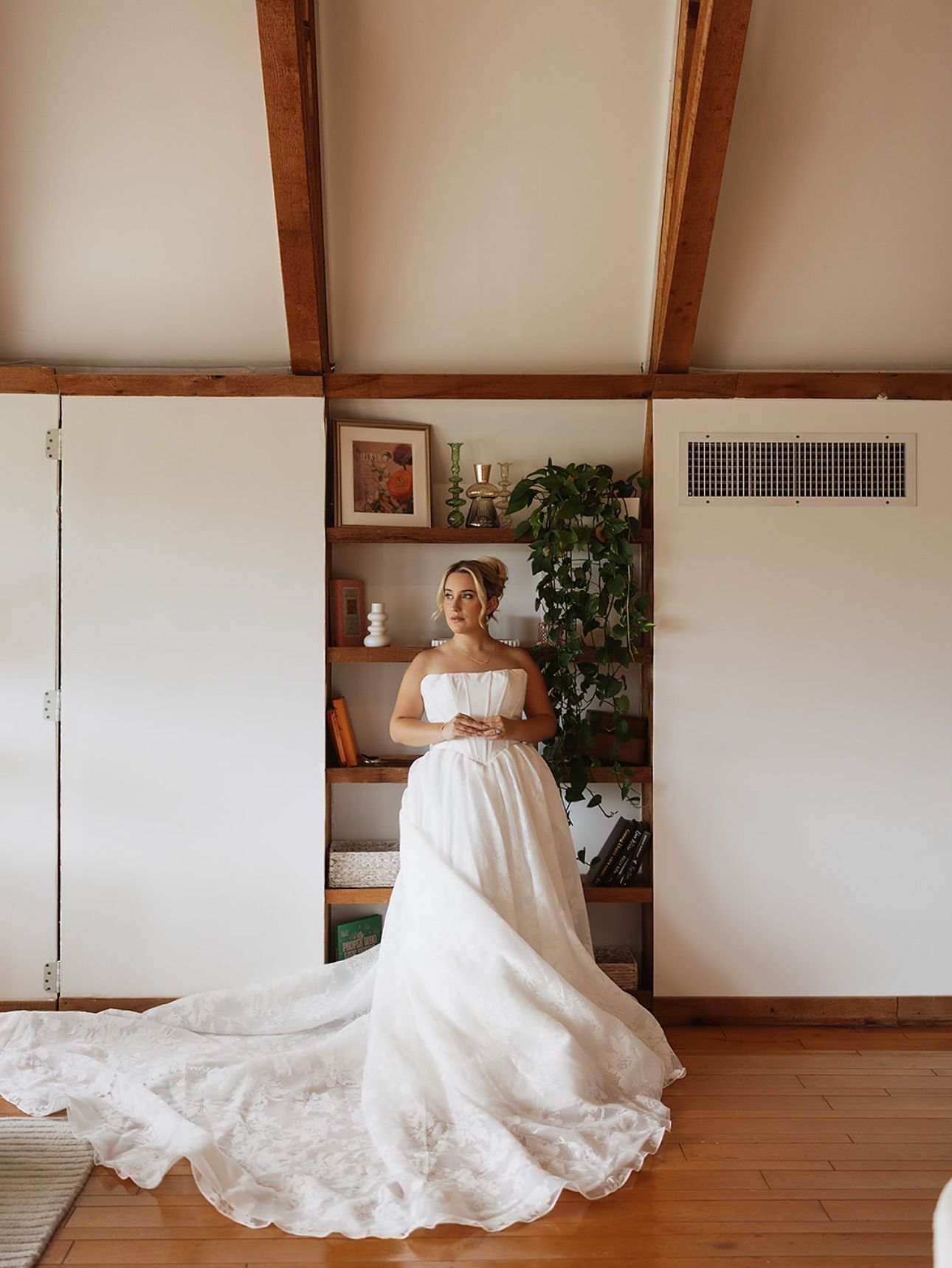 Bride in a white gown standing in front of a bookshelf, train flowing on the floor.