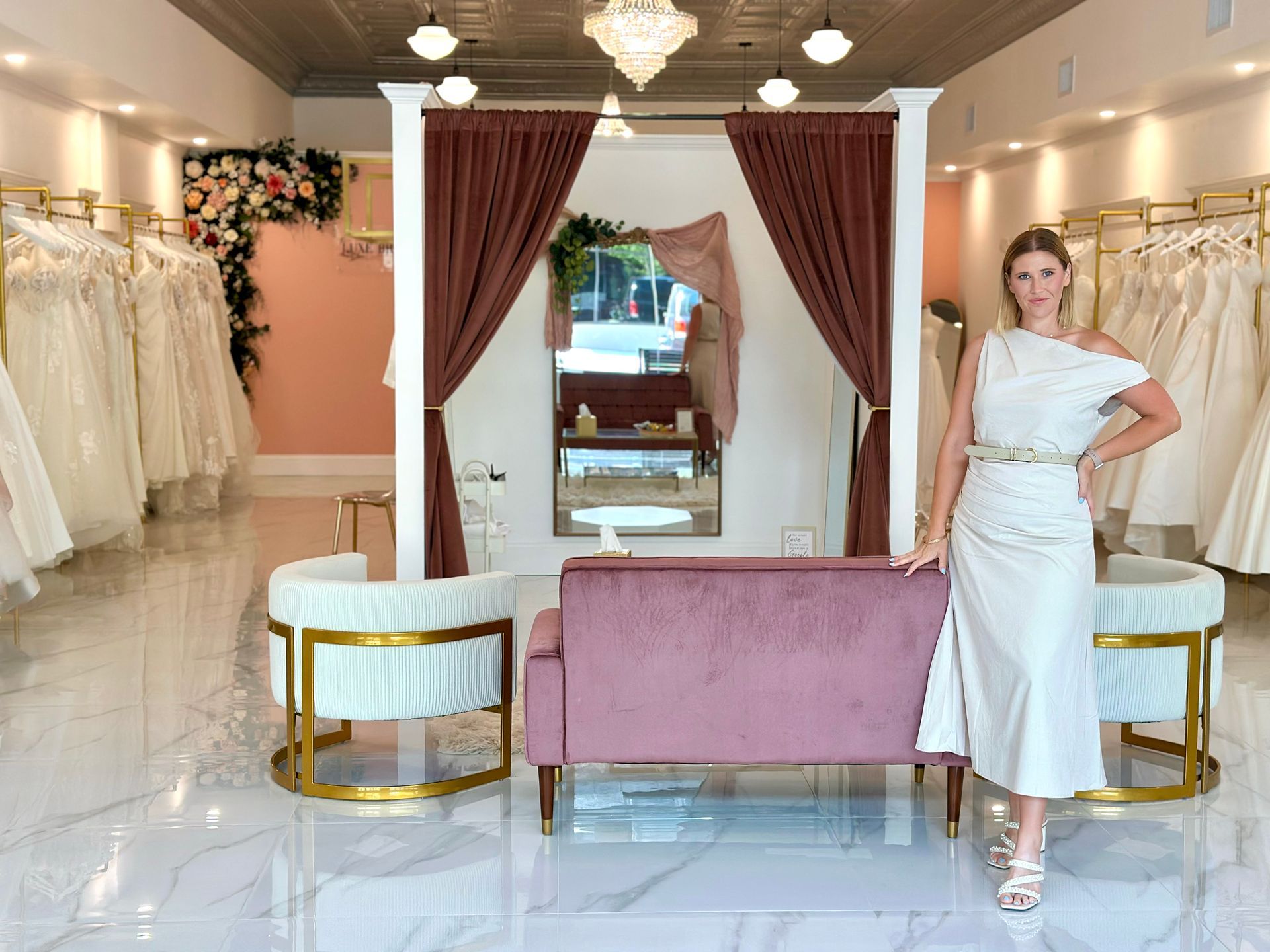 Woman in floral dress in a bridal shop, surrounded by wedding gowns.
