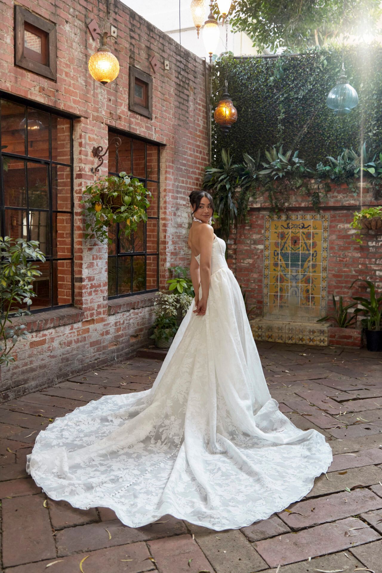 Woman in a wedding dress poses in a courtyard, a long train trailing on stone.