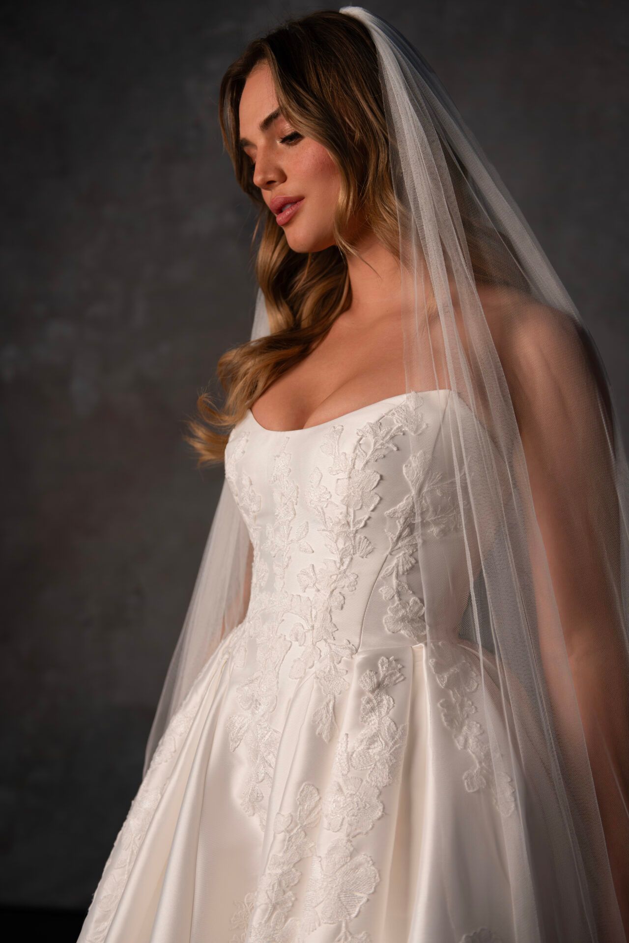 Woman in a strapless white wedding dress with lace detail, wearing a veil.