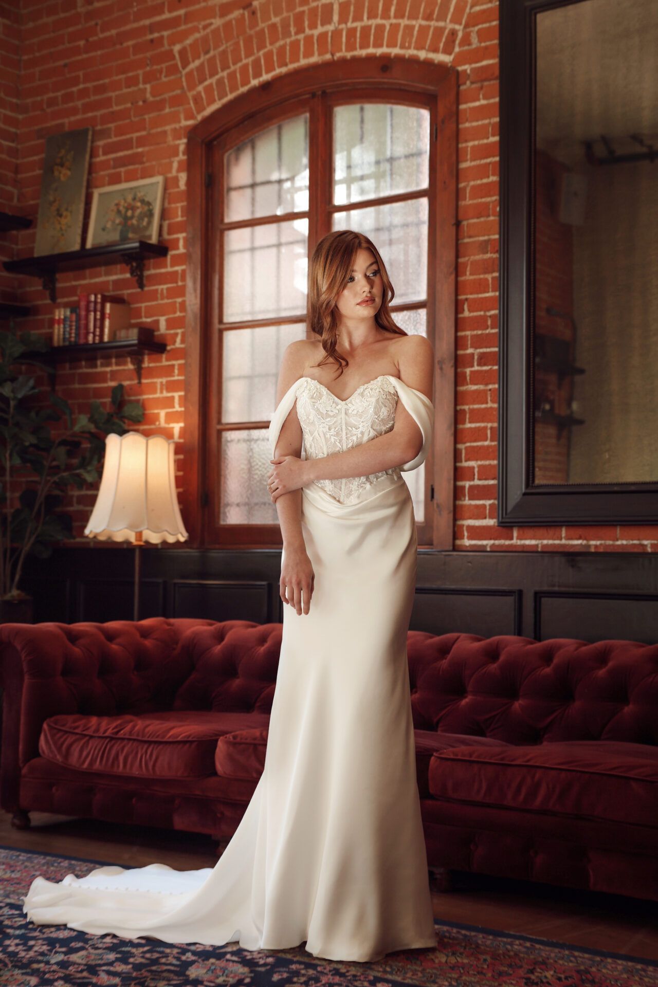 Woman in a wedding dress, standing in front of a window, indoors.