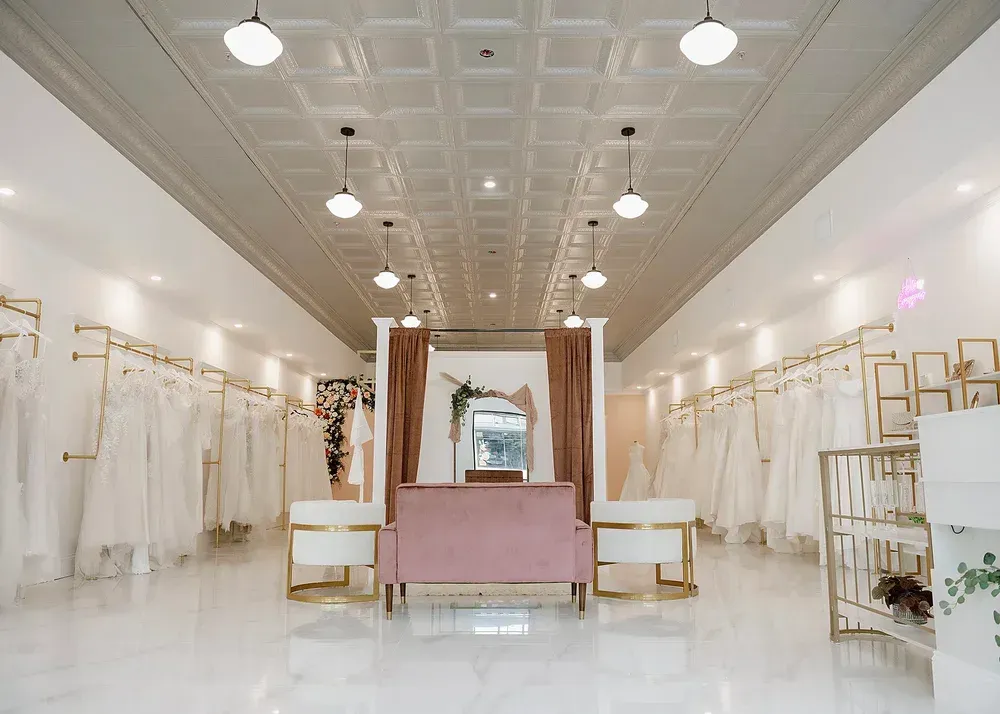 Bridal shop interior with white dresses hanging, pink velvet sofa, and gold accents.