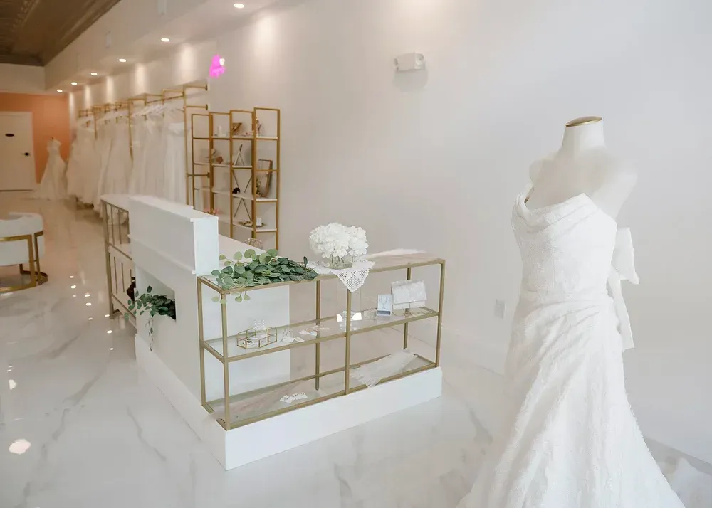 A bridal shop interior with white walls, dresses on display, and a white and gold reception desk.