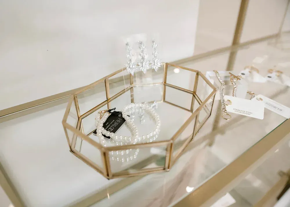 Gold geometric jewelry display with pearl bracelets and earrings on a glass shelf.