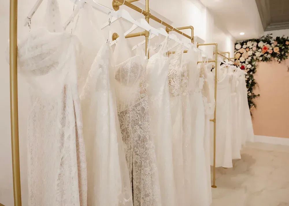 Wedding dresses hanging on a gold rod in a bridal boutique with floral decorations.
