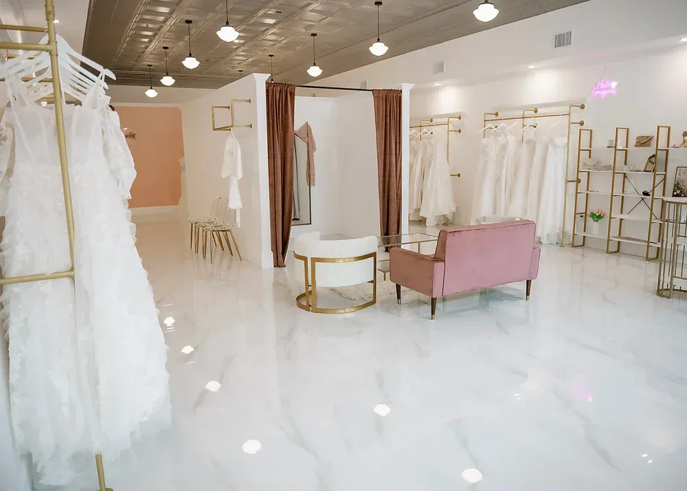 Wedding dress boutique interior with white gowns, pink accents, and a marble floor.
