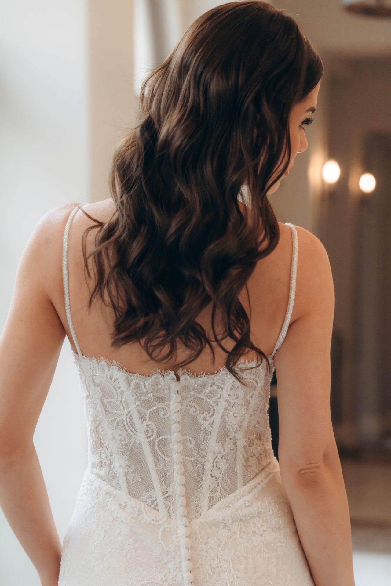 Woman in a lace wedding dress, with wavy brown hair, looking to the side.