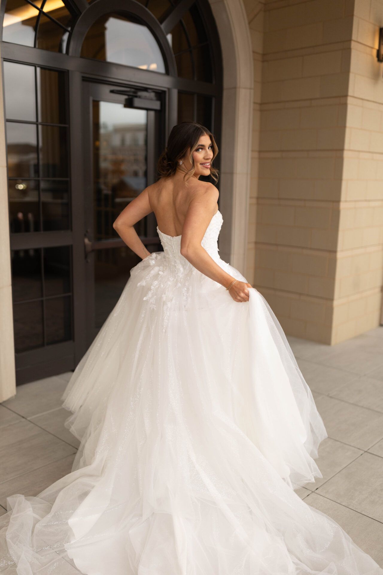 Woman in strapless white wedding dress twirling outdoors.