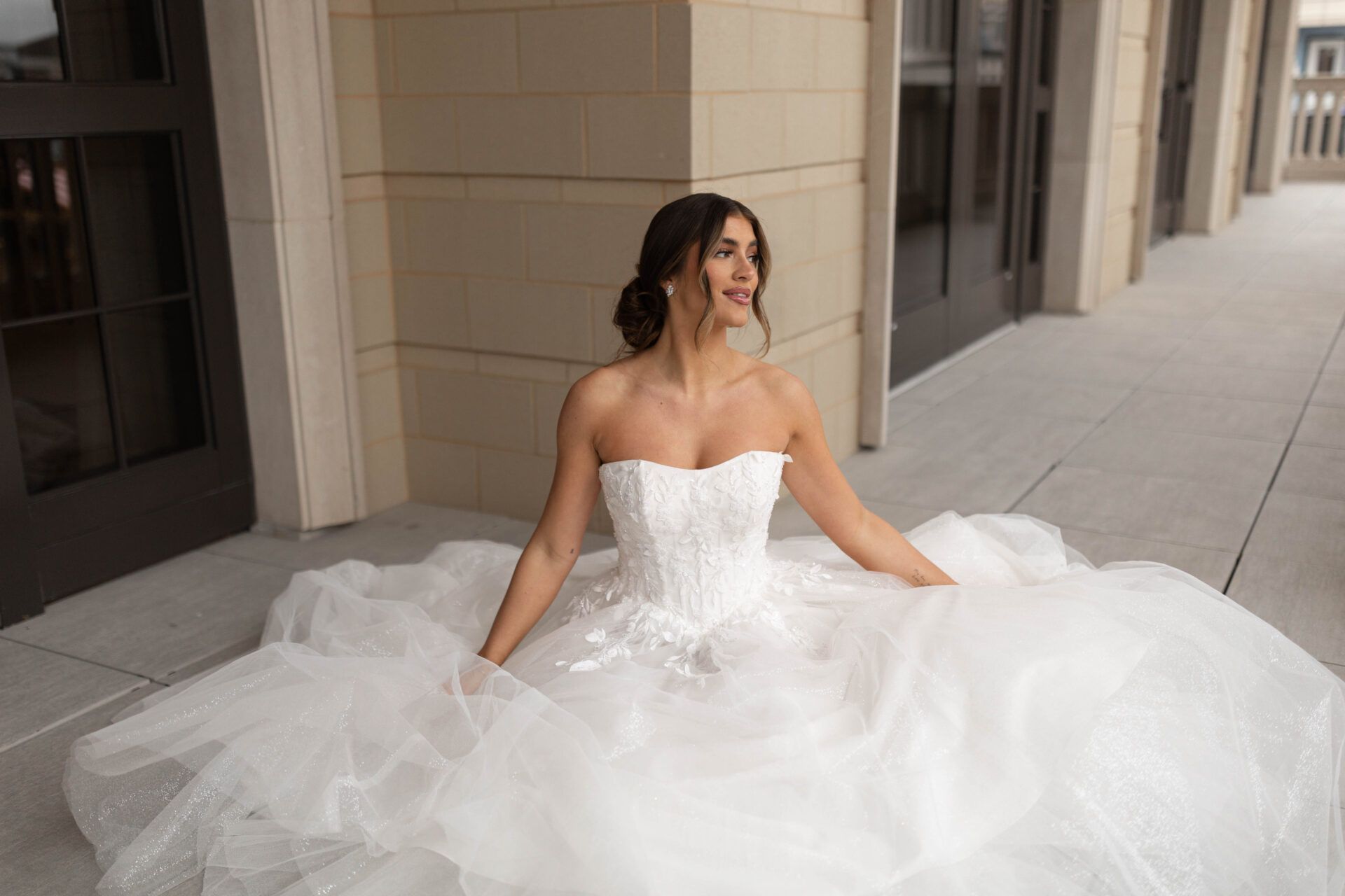 Woman in a white strapless wedding dress, seated, outdoors.
