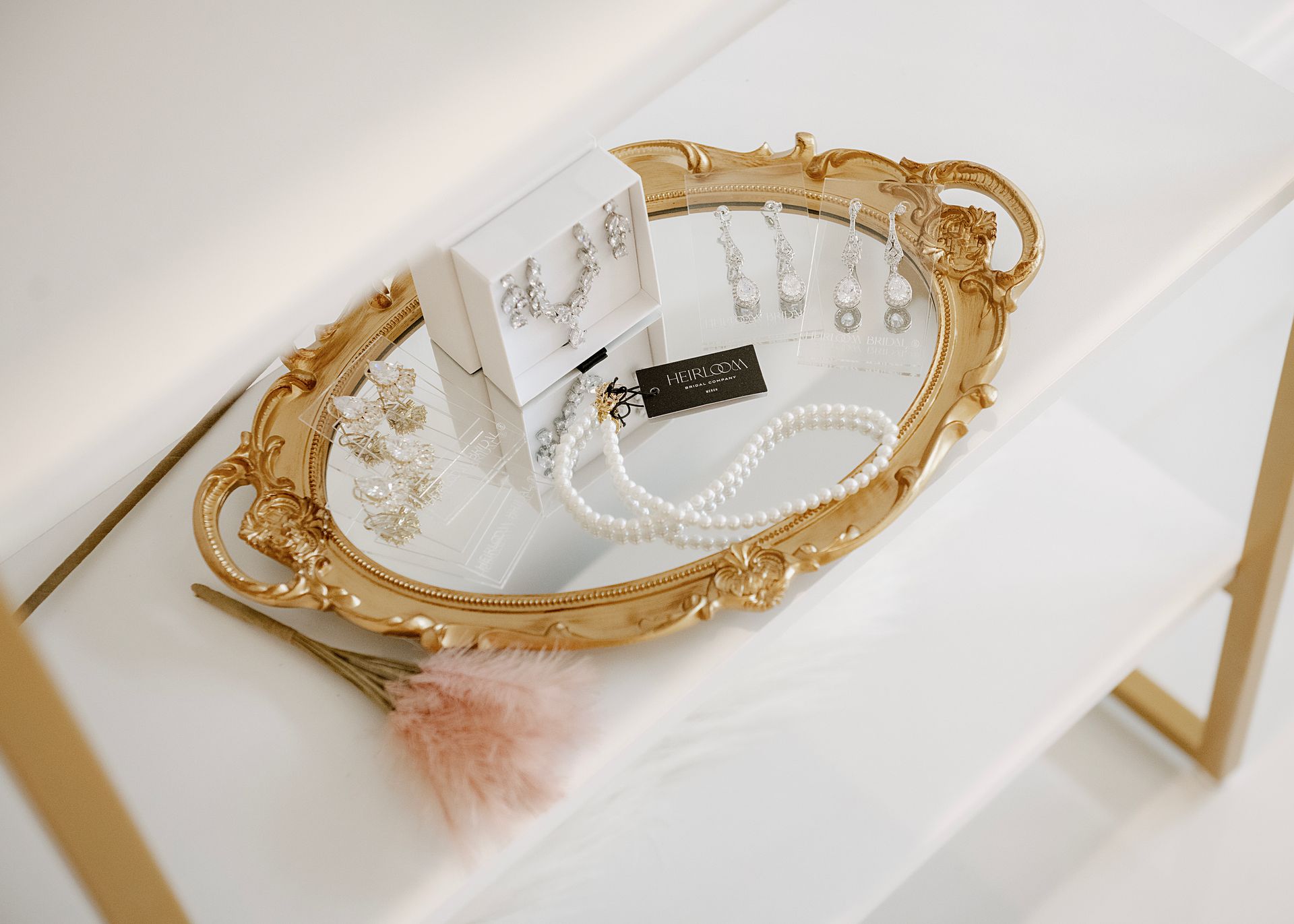 Jewelry display on a gold ornate mirror, including earrings, necklace, and a small box, on a white shelf.