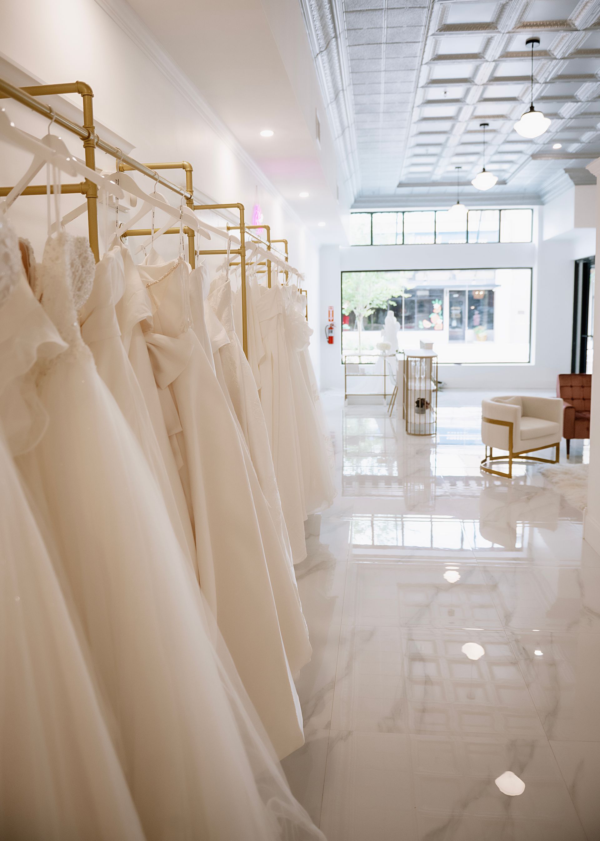 Wedding dresses hanging in a bright bridal shop with gold racks. White marble floor.