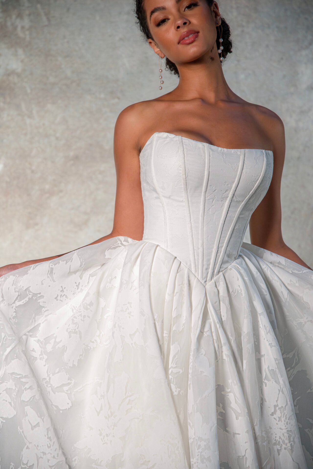 Woman in strapless white wedding dress, posing, light background.