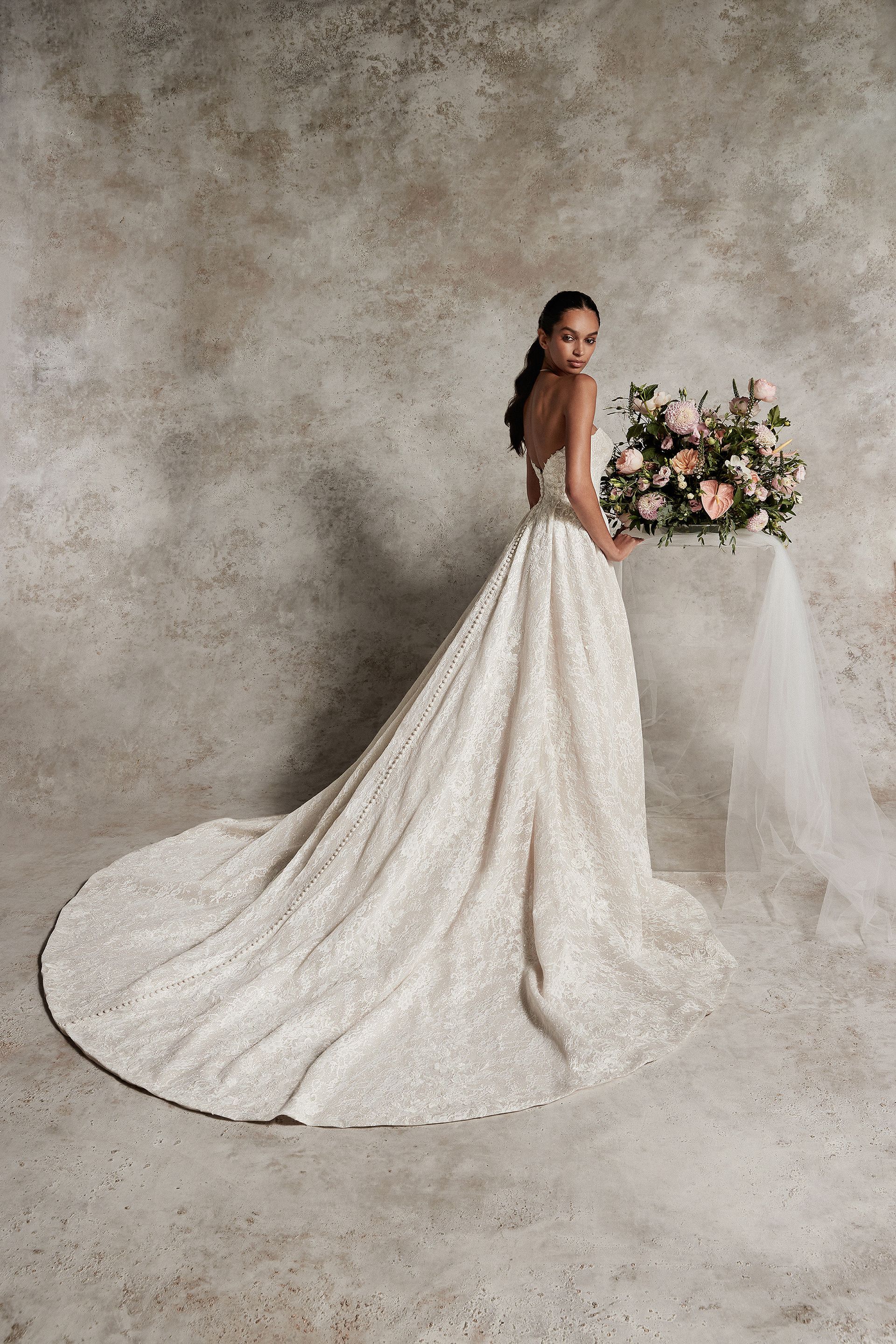 Woman in a sparkly wedding dress, holding flowers, looking over her shoulder.