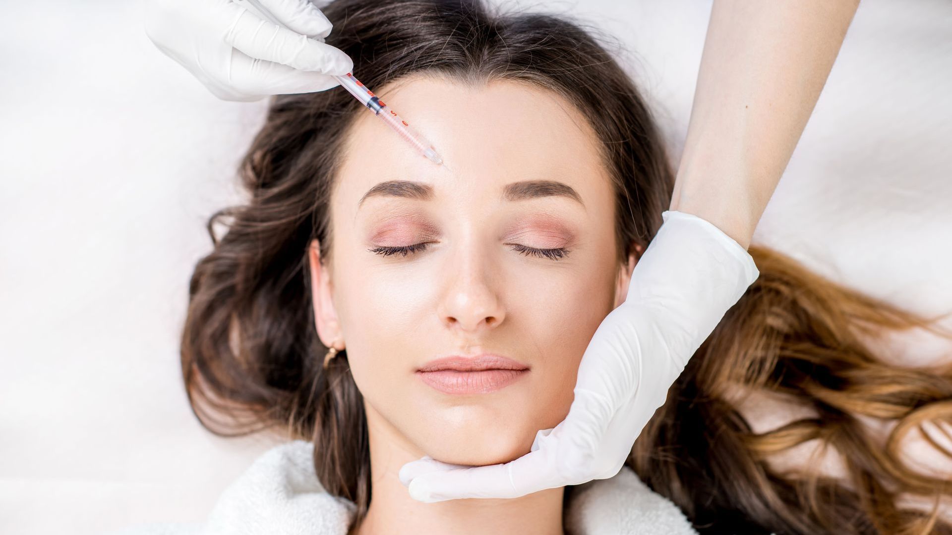 A woman is getting a botox injection in her forehead.