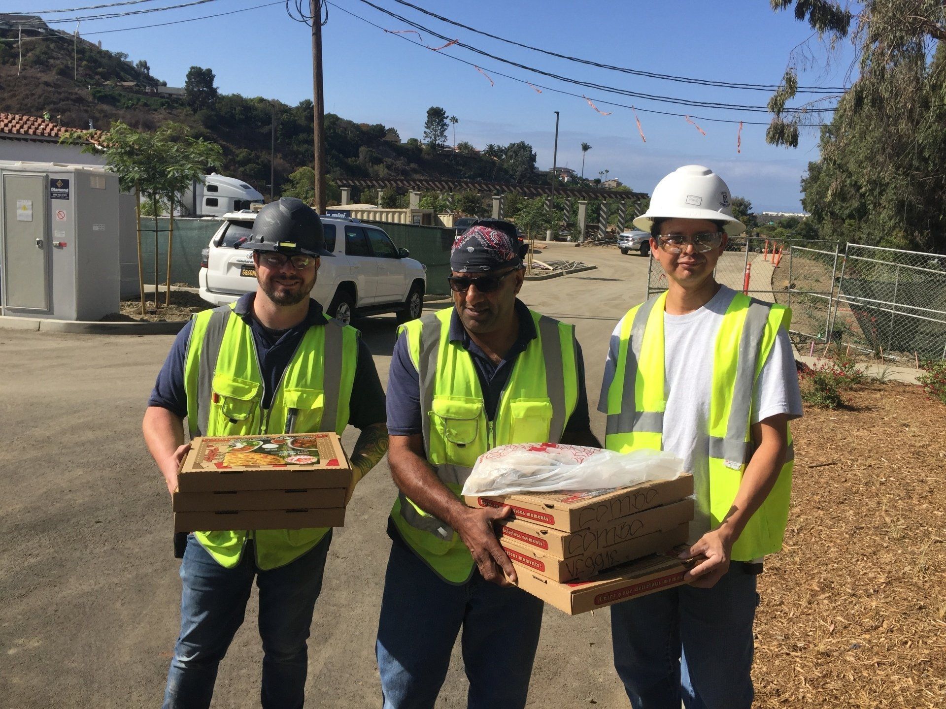 A group of construction workers are holding boxes of pizza