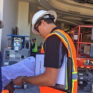 A man wearing a hard hat and safety vest is looking at a piece of paper.