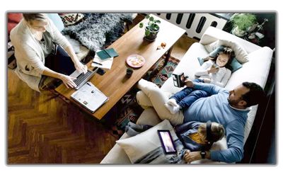 A family in a living room, with one person working on a laptop at a table and three people lounging on a sofa.