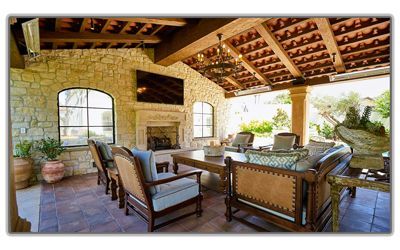 An outdoor covered patio with stone walls, a fireplace, a television, and rustic wood-framed seating on a tiled floor.