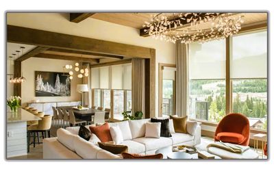 A modern, open-concept living and dining room with white sofas, warm neutral decor, wood beams, and large window views.