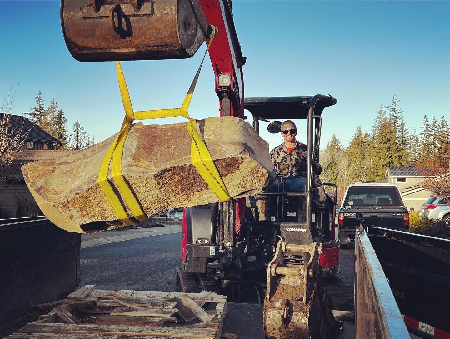 A man is driving an excavator lifting a large rock