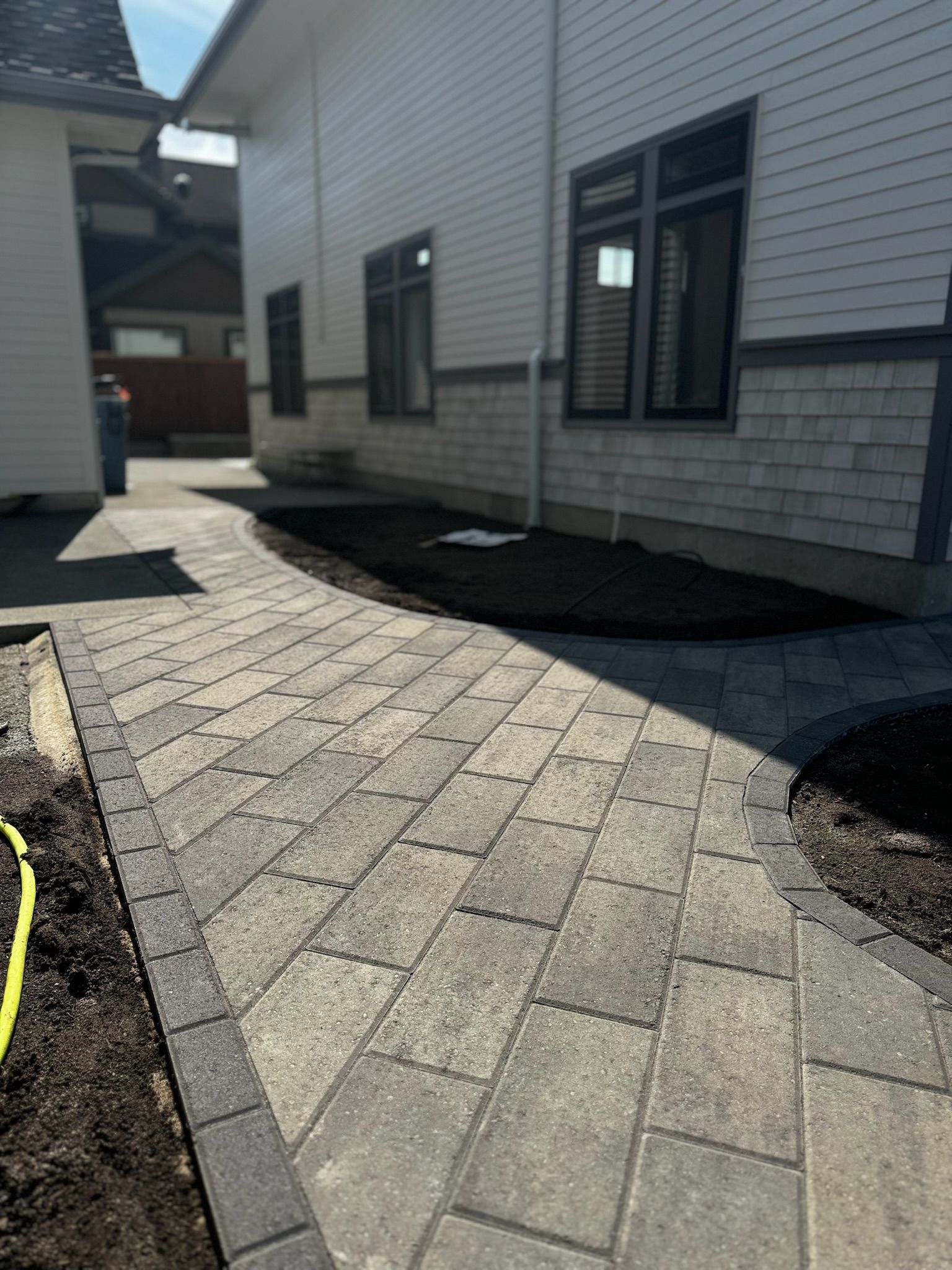 A brick walkway leading to a house with a lot of windows.
