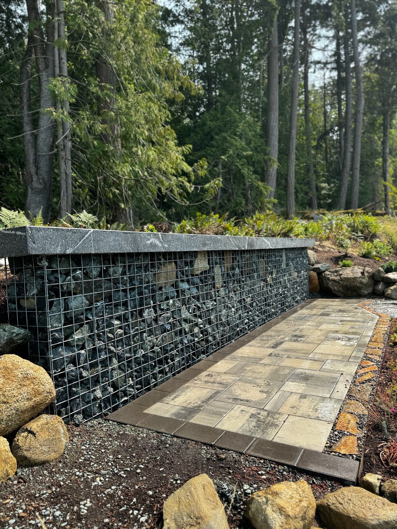 A stone wall with a walkway leading to it in the middle of a forest.