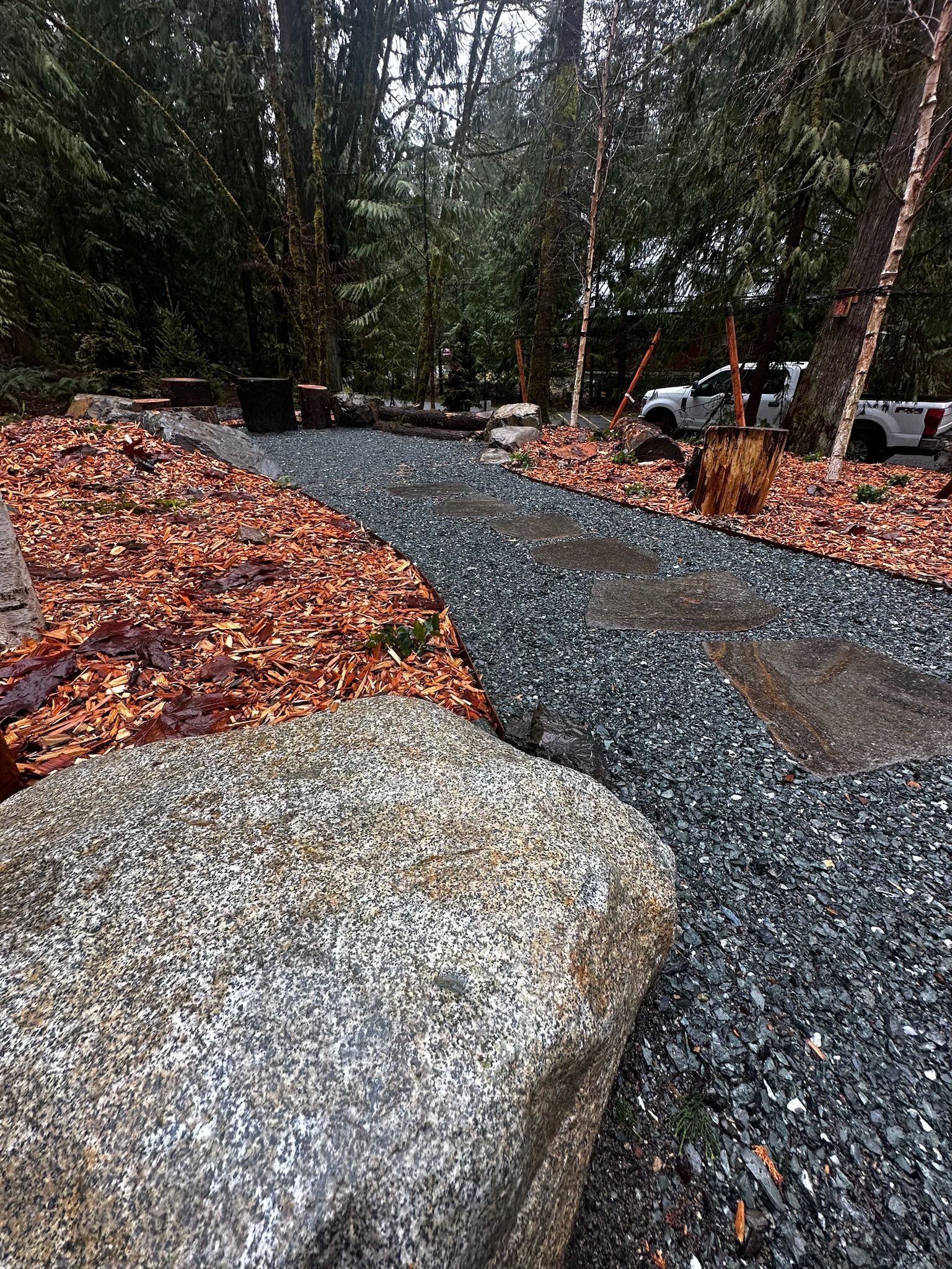 A gravel path in the woods with a large rock in the middle.